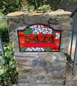 House number sign with dogwood blossoms against a red glass background. Fused glass and mosaic art.