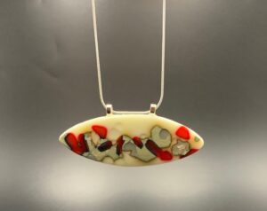 Fused glass red and silver surfboard shaped pendant with a cream background.