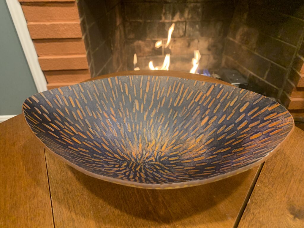 Orange and blue fused glass oval bowl with patterns on the top and bottom.