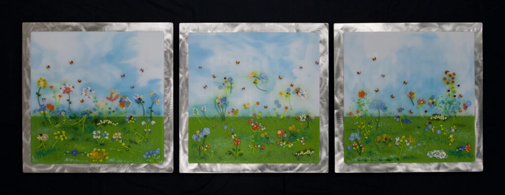 Three fused glass panels depicting meadows mounted on stainless steel frames.