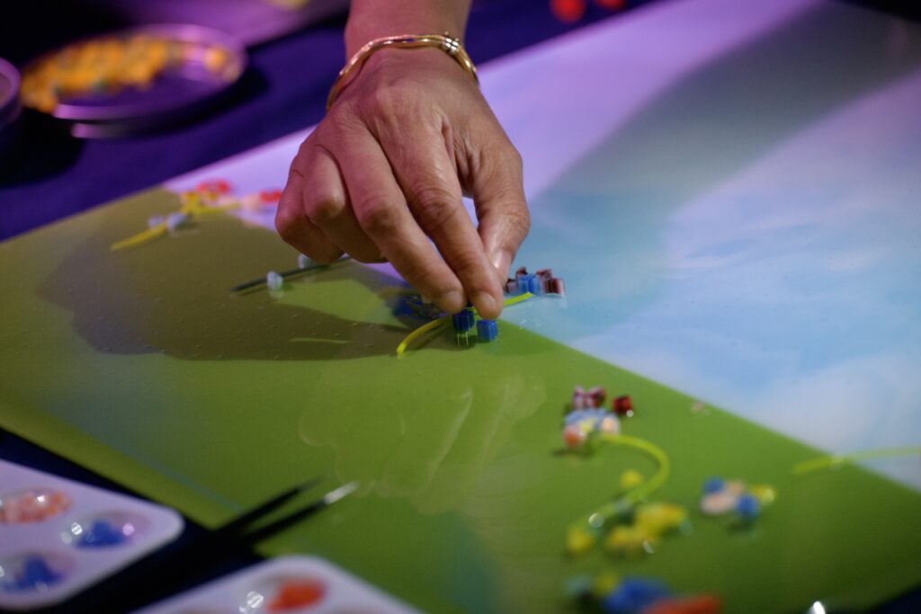 A hand placing a glass piece on the art panel.